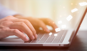 Person typing on a laptop with digital envelope icons symbolizing email or automated mail sending