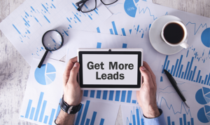 Tablet with the words “Get More Leads” held above scattered analytics documents and graphs.