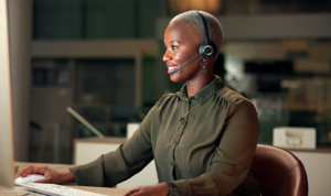 Smiling support agent with headset using a desktop computer in an office setting