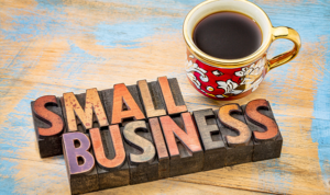 Wooden block letters spelling “Small Business” beside a coffee mug on a wooden desk.