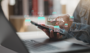 Person holding smartphone with floating local business icons and “Local SEO” overlay in front of a laptop