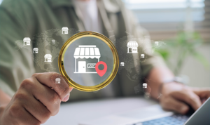 Person holding a magnifying glass over digital storefront icons and location pins on a global map background