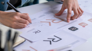 Designer sketching and reviewing logo drafts and typography layouts on paper during concept development.