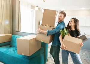 Happy couple carrying boxes into their new home, symbolizing the moving transition period.